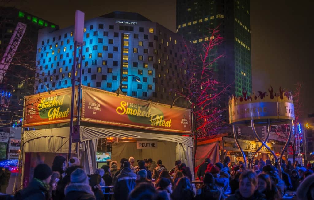 A festival environment in a city at night with various colored lights projecting across buildings