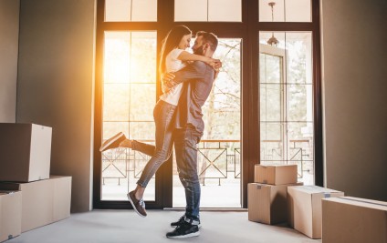 Happy couple with cardboard boxes in new house at moving day.