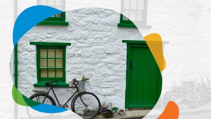 A bike sits in front of a white stone house with a green door and trim