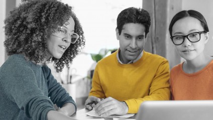 Two women and one man with brightly colored shirts collaborating around a computer