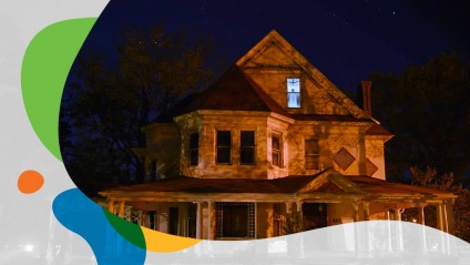 A large older home with shadowy lighting and a creepy scene in the upstairs window