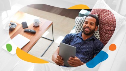 A smiling man laying on a couch looking at a tablet