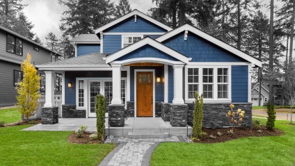 Front view of house with landscaped front yard, blue exterior walls with grey stone an white columns