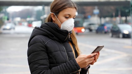 A young woman wearing a face mask looking down at her phone