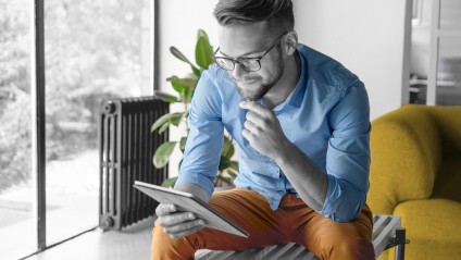 Young man with glasses, a blue shirt and orange pants browsing on a tablet