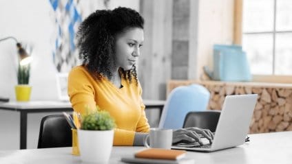 A young female with a bright yellow shirt working on her laptop