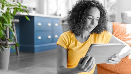 A young female in a yellow shirt sitting on the floor while browsing a tablet