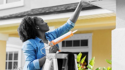 Woman fixes a rain gutter using a caulking gun on a ladder