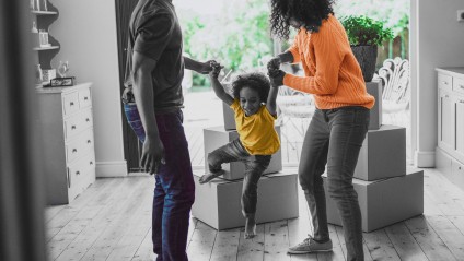 Mom and dad playing with child in front of moving boxes in a home.