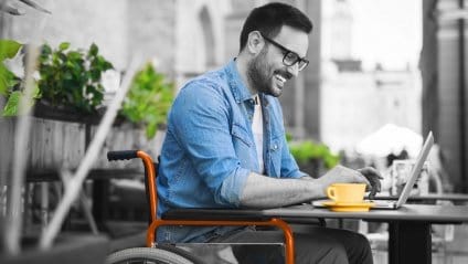 man sitting in a wheel chair smiling and looking at laptop