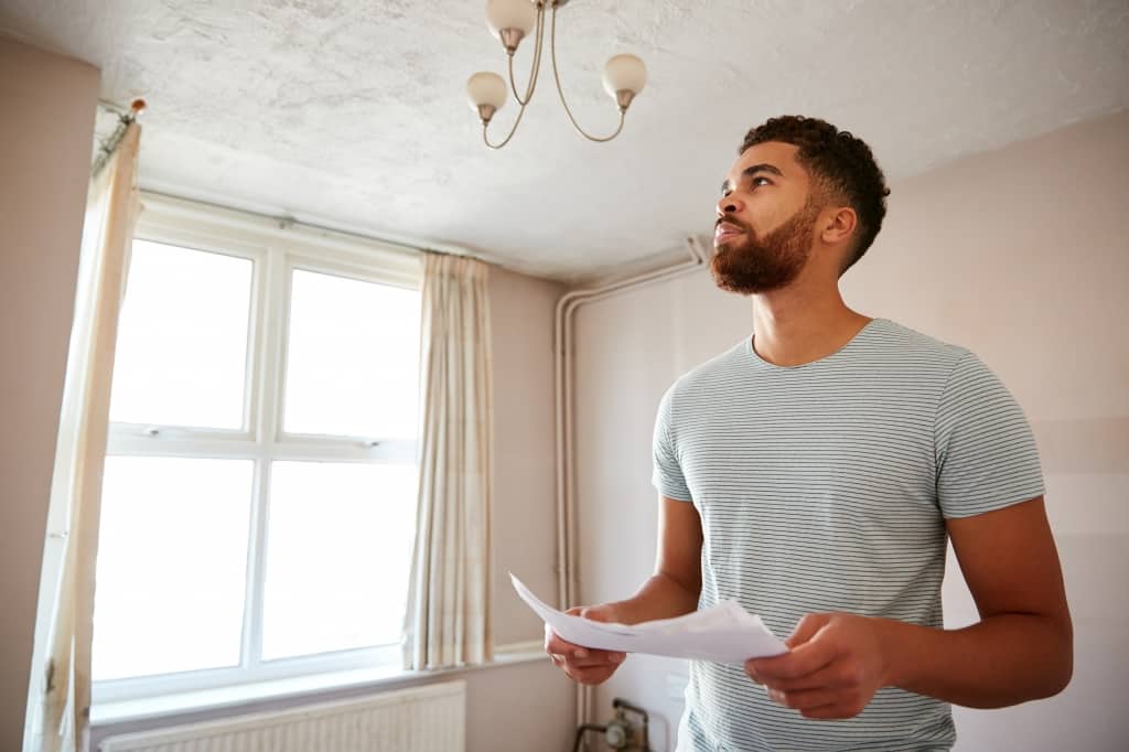 Male First Time Buyer Looking At House Survey In Room To Be Renovated