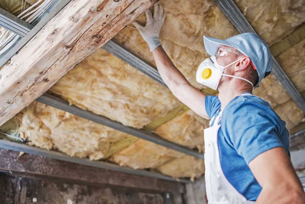 Construction Worker in His 30s Inspecting Aged Roof and Mineral Wool Insulator