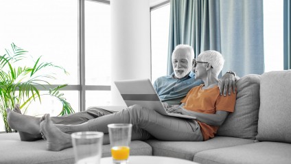 elderly couple relaxing on couch while looking at a laptop