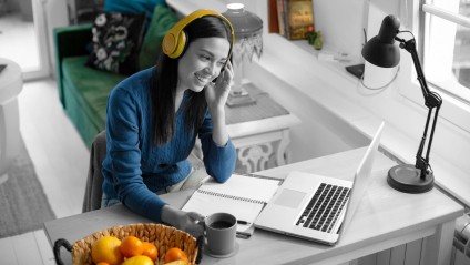 woman with headphones sitting at her work desk smiling at her laptop