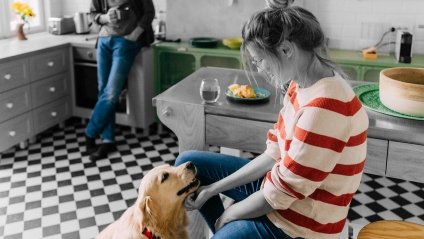 woman in red and white striped shirt petting her golden retriever dog in the kitchen