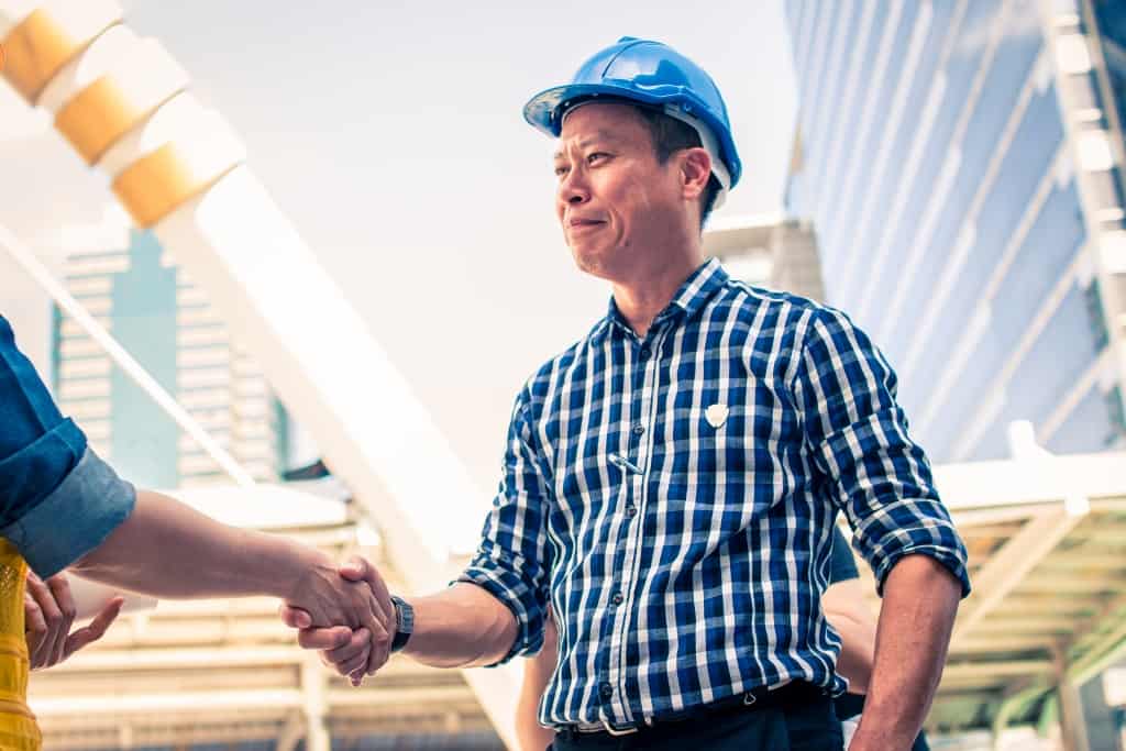 Construction worker in protective uniform shaking hands meeting for architectural project working with partner.