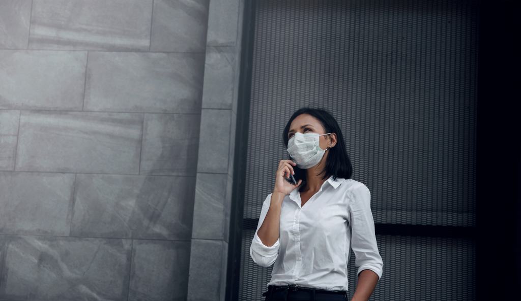 Business Woman with Medical Mask Looking Up while Using Smartphone.