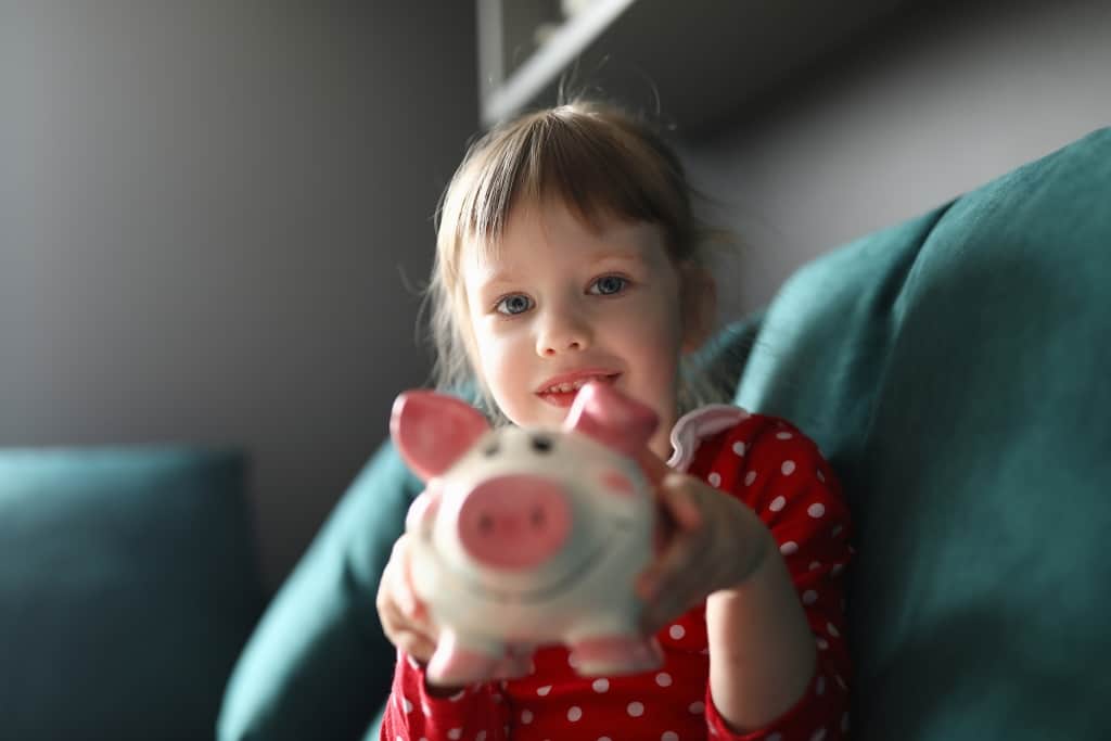 Child hold pink piggy bank in her hands and show