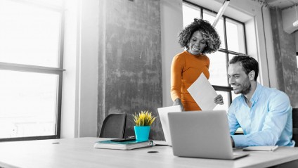 man and woman working in an office smiling at the laptop