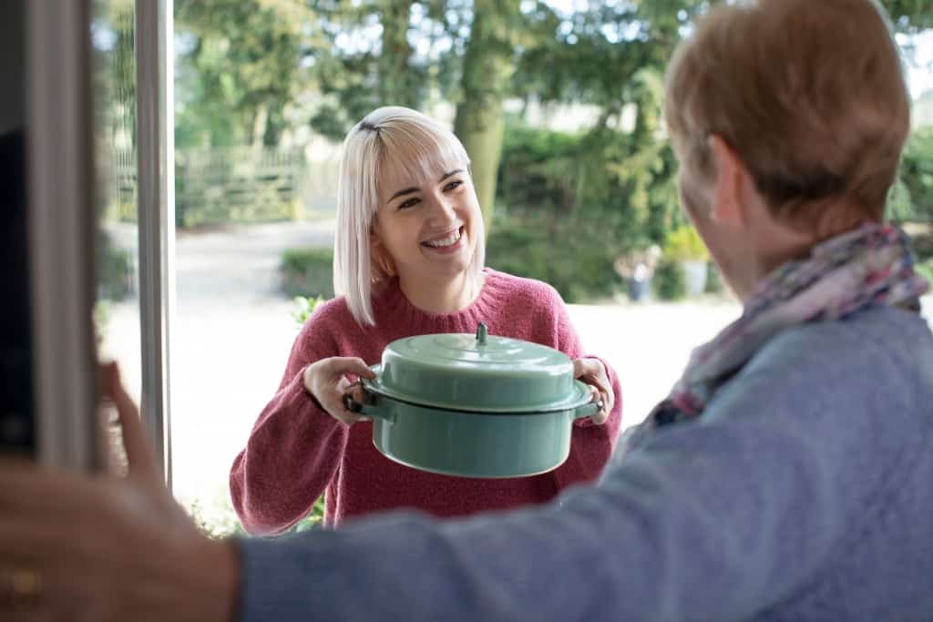 Young Woman Bringing Meal For Elderly Neighbour