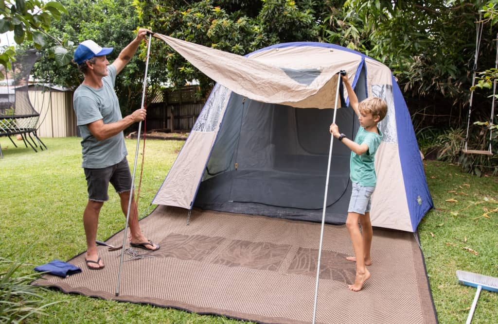 son and father setting up tent in their back yard while wearing blue t shirts shorts and flipflops