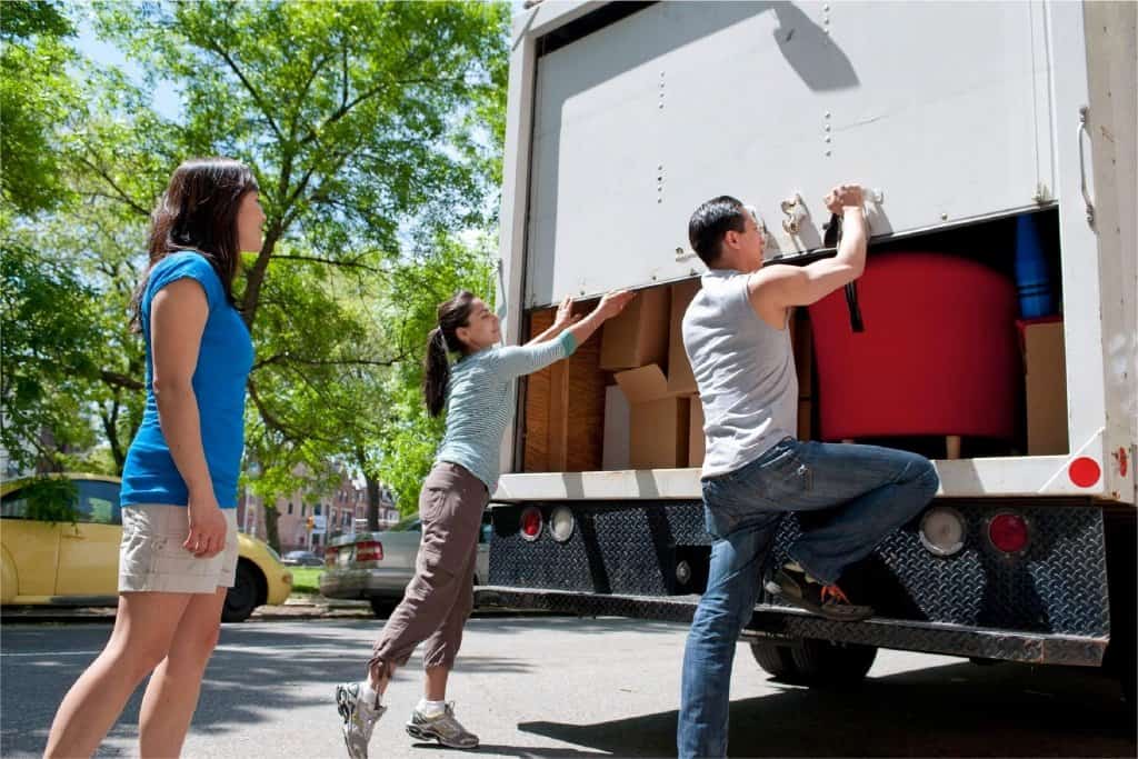 A male and female closing the back door of a moving truck full of boxes and furniture