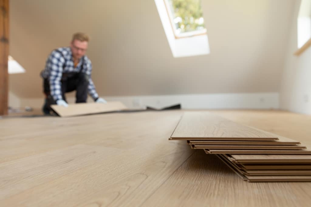 Construction worker installing laminate floor as a COVID-friendly DIY in a new renovated attic