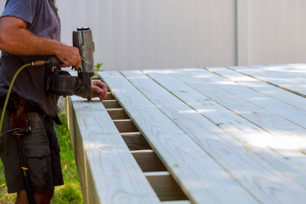 Building a backyard deck with worker putting with nail gun deck boards terrace patio construction.