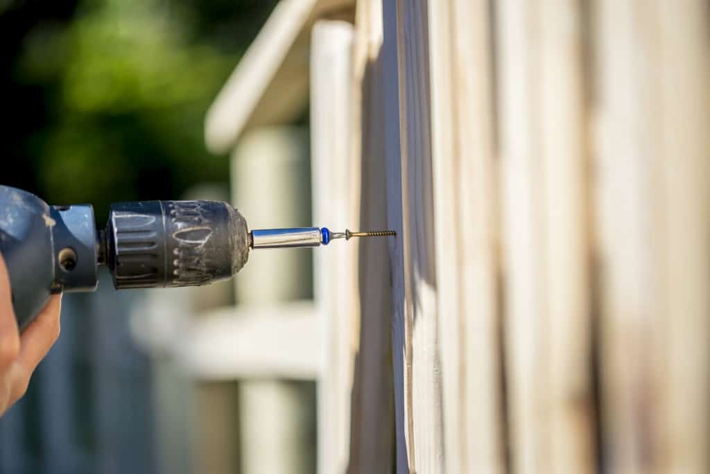 Person building a wooden fence with a drill and screw using a hand held power drill in a concept of yard maintenance renovations and DIY.