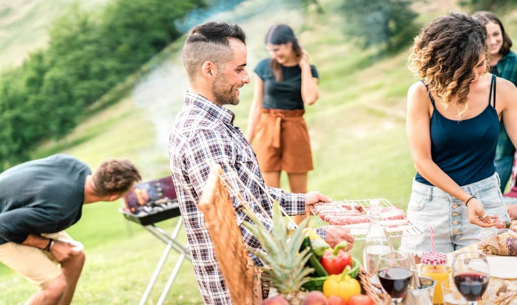 Young friends having fun on outdoors picnic preparing food at barbecue grill party