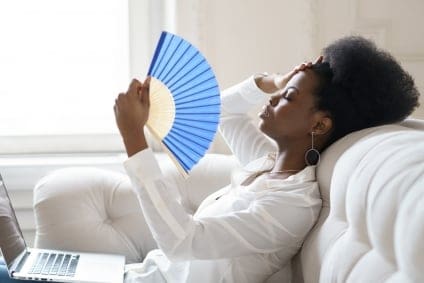 Black woman using a fan while sitting on her couch to keep cool