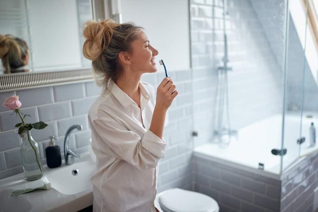 Young handsome girl brushing teeth on a beautiful morning in the bathroom. Hygiene, bathroom, morning