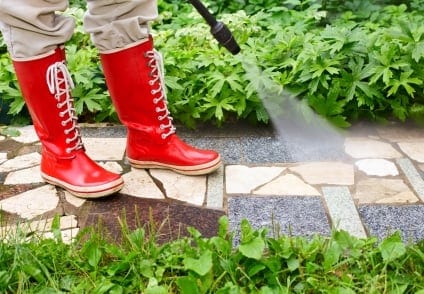 person in red rubber boots pressure washing walkway