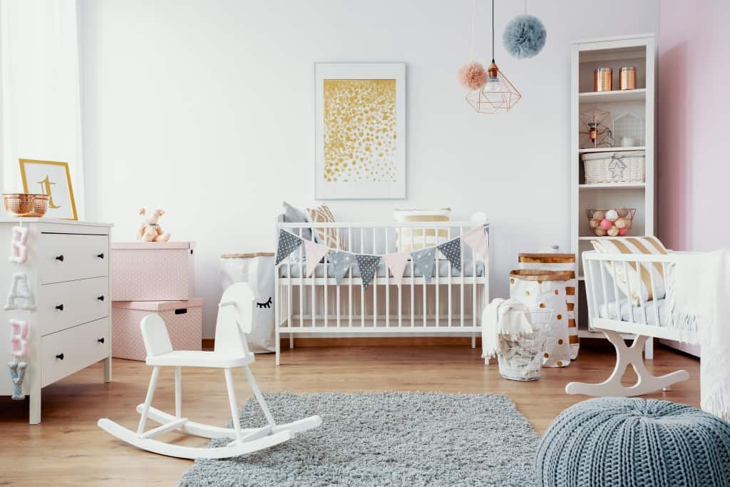 Bright baby room with white furniture, grey carpet on the floor and golden painting on the empty wall, real photo