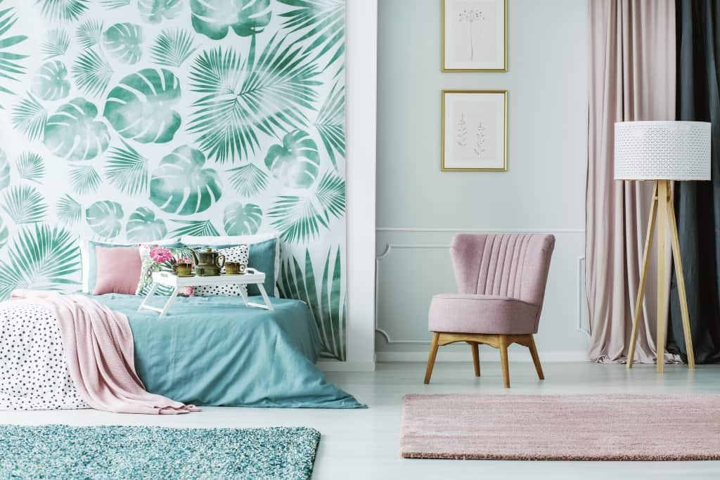 Pink chair next to white lamp in pastel bedroom interior with posters and green leaves wallpaper