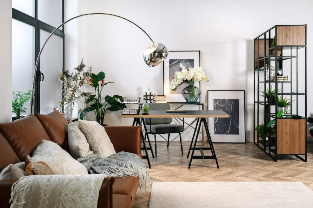 Home office in living room with modern interior design, comfort sofa, laptop computer, paper documents on work desk near armchair