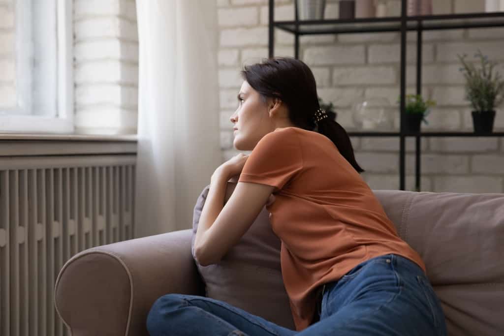 Upset thoughtful young woman sitting on couch, looking to aside