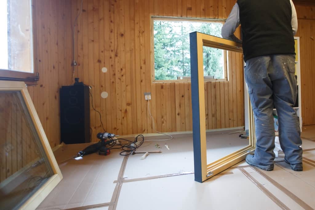 Worker preparing to install new three pane wooden windows in an old wooden house
