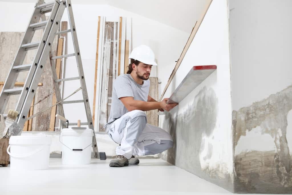 construction worker plasterer man looks at the spirit level and checks the wall in building site of home renovation with tools and building materials on the floor
