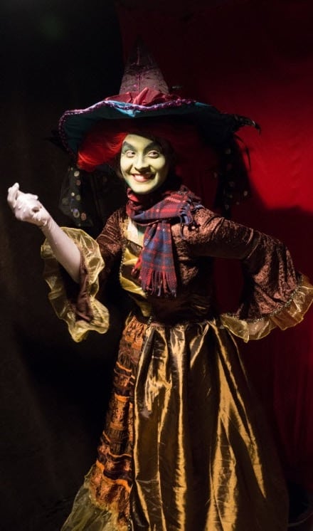 Eerie image of grinning woman dressed as a witch in front of a sinister background