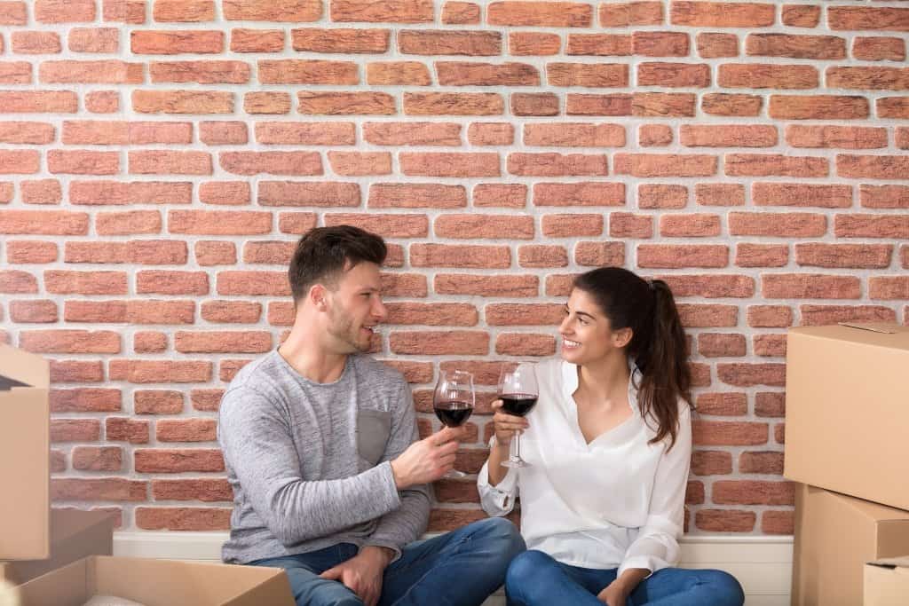 a man and woman celebrating by drinking wine in wineglasses with unpacked boxes near them