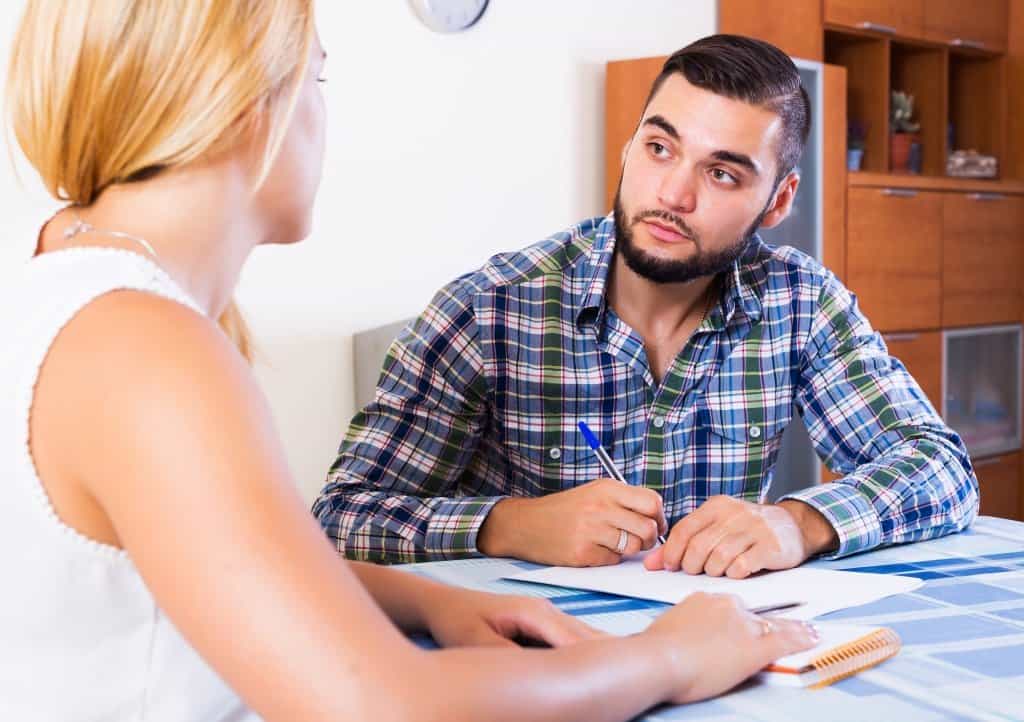 a man takes notes while a woman is talking to him