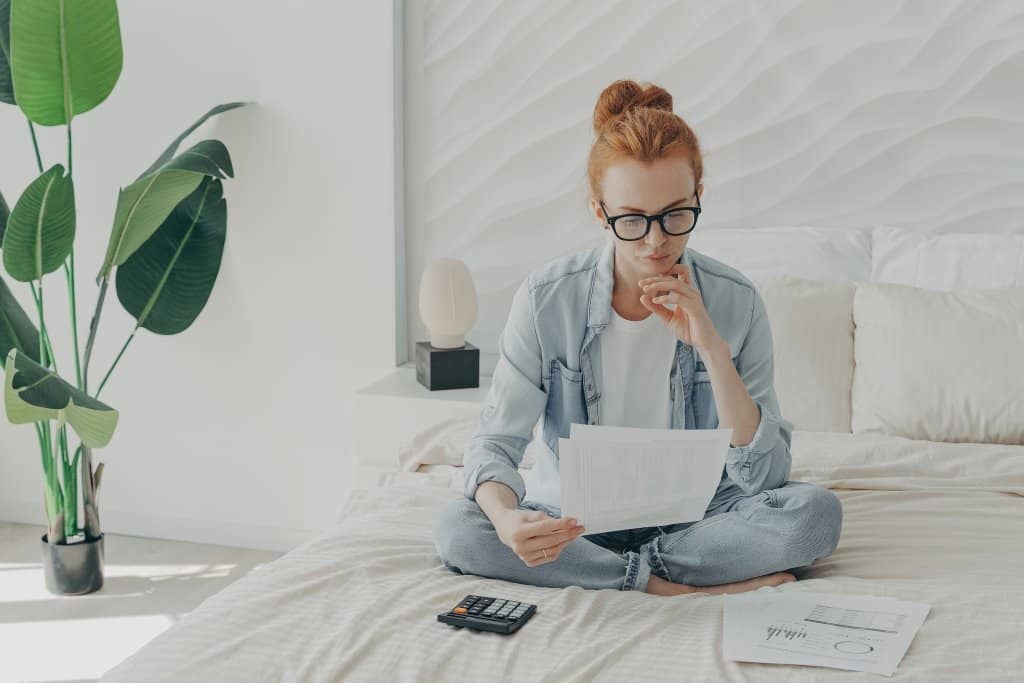 a woman reads papers while sitting on a bed