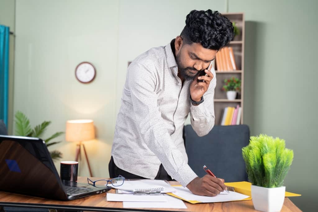 a man is speaking on the phone and taking notes in his home office