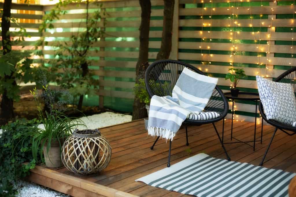 A wooden deck or patio with outdoor seating and fairy lights on the trellis in the background