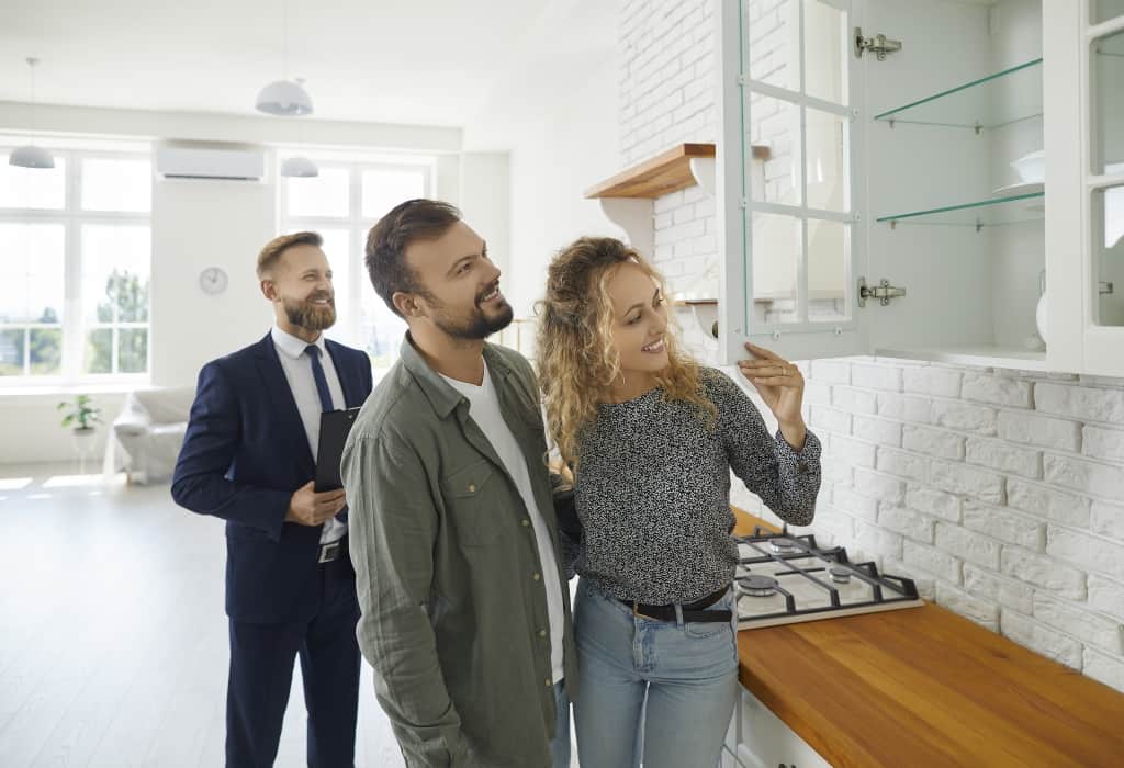 a man and woman look at kitchen cabinets with a male real estate agent